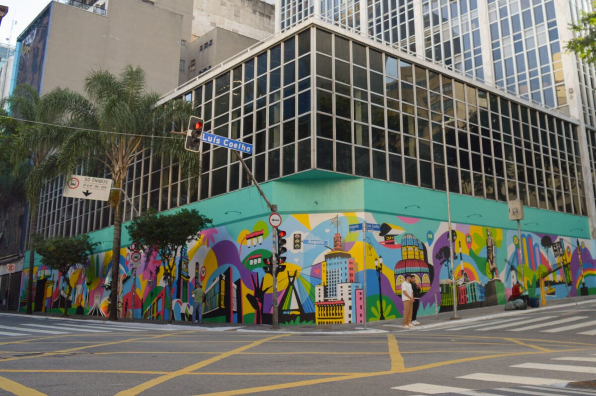 Mural colorido representando monumentos brasileiros com pedestres caminhando na Rua Augusta, em São Paulo.