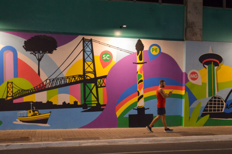 Mural colorido representando monumentos brasileiros com pedestres caminhando na Rua Augusta, em São Paulo.